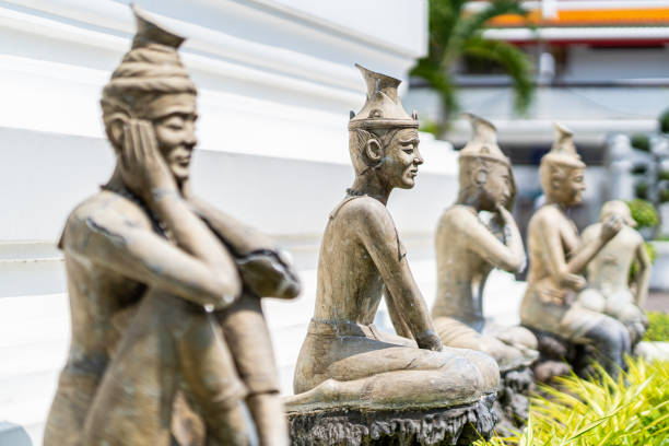 Row of traditional Thai-style meditation statues sitting in relaxed poses outside a bright white temple wall.